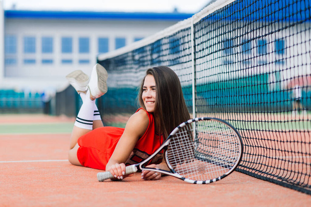 Όμορφη γυναίκα τενίστρια στο γήπεδο τένις με κόκκινο φόρεμα. - Φωτογραφία, εικόνα