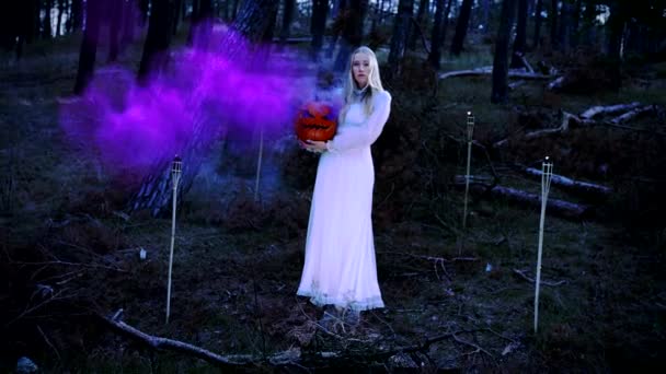 mooi blond jong meisje in een wit jurk houden een pompoen met paars rook - Video