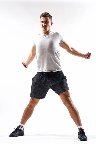 A sports man in shorts and a full-length T-shirt does exercises on a light background - Foto, Bild