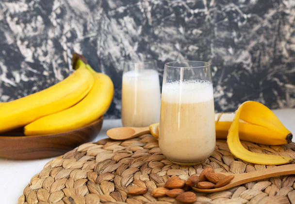 Smoothie plátano saludable en tablero de madera con leche de almendras sobre fondo blanco y gris, bebida cruda vegana - Foto, imagen