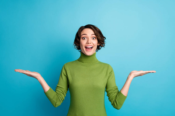 Portrait of astonished girl promoter demonstrate incredible ads promotion hold hand impressed wear green jumper isolated blue color background - Foto, immagini