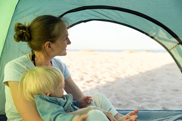 Mamma sorridente con bambino riposo nella tenda turistica. Vista mare e spiaggia. Vacanza con bambini. - Foto, immagini