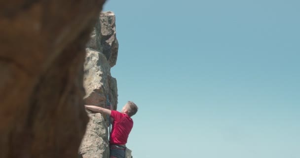 Hombre alcanzando la cima de las rocas de la montaña - Imágenes, Vídeo