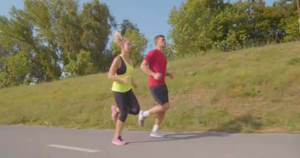 Νεαρό ζευγάρι τρέχει τζόκινγκ σε ασφαλτοστρωμένο δρόμο στο πάρκο - Πλάνα, βίντεο
