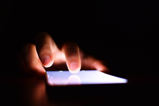 Nahaufnahme einer Person, die ein Smartphone mit beleuchtetem Bildschirm in der Dunkelheit benutzt - Foto, Bild