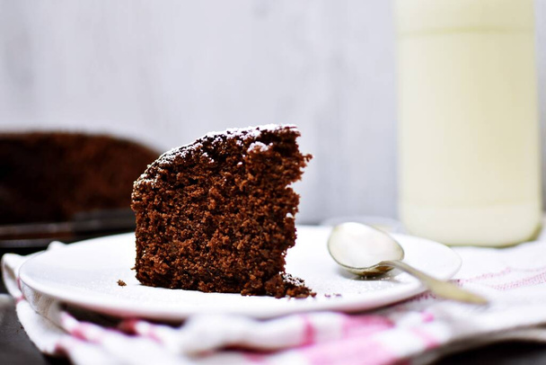 Un morceau de gâteau au chocolat maison sur une assiette de couleur claire - délicieux gâteau au chocolat avec du lait et du café sur une table, pour le café de l'après-midi - Photo, image
