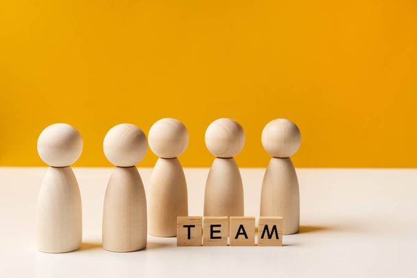 Company of wooden people on a yellow background with letters. The concept of team work and management, copy space - Valokuva, kuva