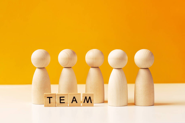 Company of wooden people on a yellow background with letters. The concept of team work and management, copy space - Foto, Imagen