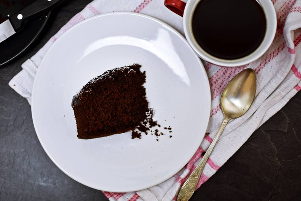 Ένα κομμάτι σπιτικού κέικ σοκολάτας σε ένα ανοιχτόχρωμο πιάτο - νόστιμο, κέικ σοκολάτας με γάλα και καφέ σε ένα τραπέζι, για τον απογευματινό καφέ - Φωτογραφία, εικόνα