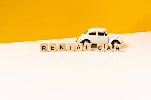 Brinquedo carro branco em uma mesa branca com um fundo amarelo, a inscrição de blocos de madeira. O conceito de um carro alugado e compartilhamento de carro. - Foto, Imagem