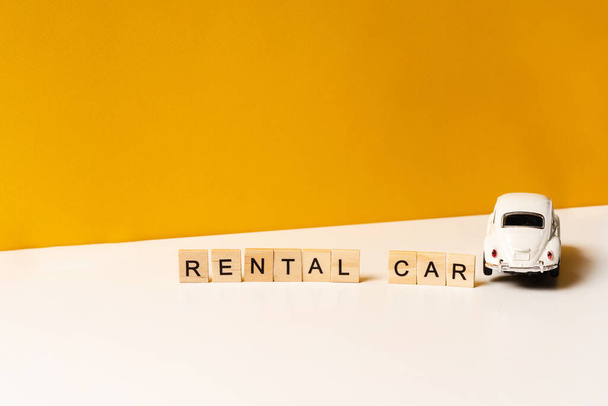 Zabawkowy biały samochód na białym stole z żółtym tłem, napis drewnianych klocków. Koncepcja wynajmu samochodu i wspólnego korzystania z samochodu. - Zdjęcie, obraz