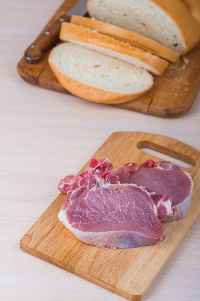 Tahta kesme tahtasının üzerinde domuz eti var. Eski bir tahta kesme tahtasının üzerinde bir somun beyaz buğday ekmeği yatıyor.. - Fotoğraf, Görsel
