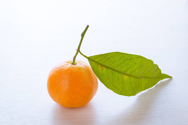 A ripe tangerine with green leaf on a table. - Photo, Image