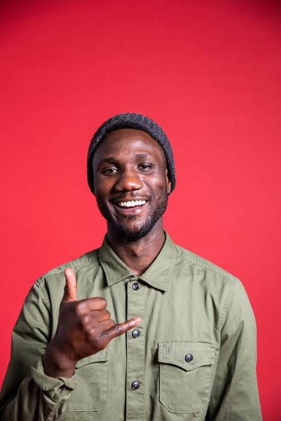 Young black man with toothy smile showing the call me hand sign. Isolated background. Medium shot. Looking at camera.  - Photo, Image