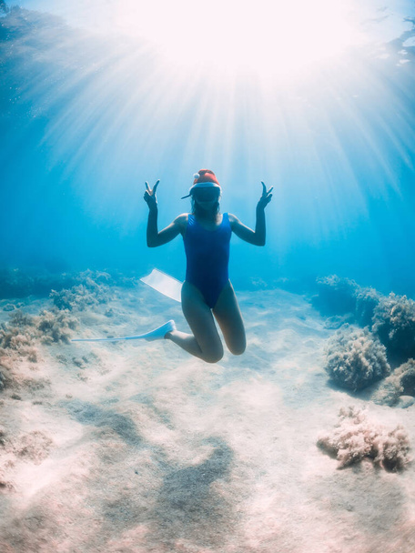 Szczęśliwa kobieta freediver z czapką noworoczną ślizga się pod wodą w błękitnym oceanie. Koncepcja świąt Bożego Narodzenia - Zdjęcie, obraz