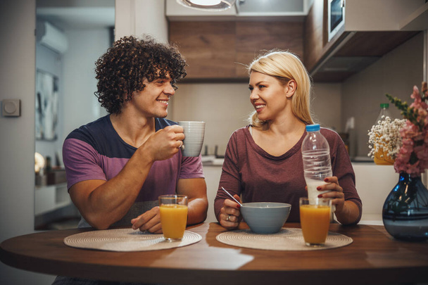 幸せなカップルのショット一緒に朝食を食べ、自宅でキッチンで話す. - 写真・画像