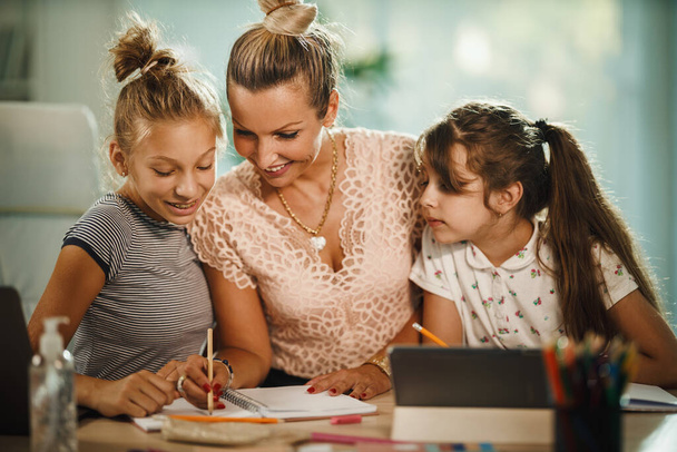 Girato di una bella giovane madre che aiuta le sue due figlie con i compiti durante la pandemia del COVID-19. - Foto, immagini