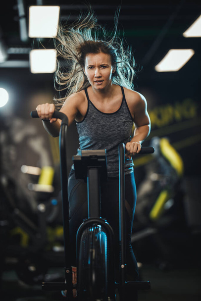 Młoda muskularna kobieta trenuje na siłowni na rowerze treningowym. - Zdjęcie, obraz