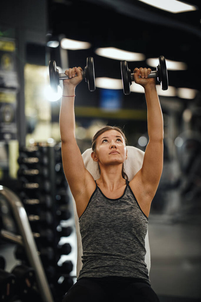 Знімок м'язистої молодої жінки в спортивному одязі, що працює на важкій підготовці в спортзалі. Вона накачує м'язи плеча з великою вагою
. - Фото, зображення