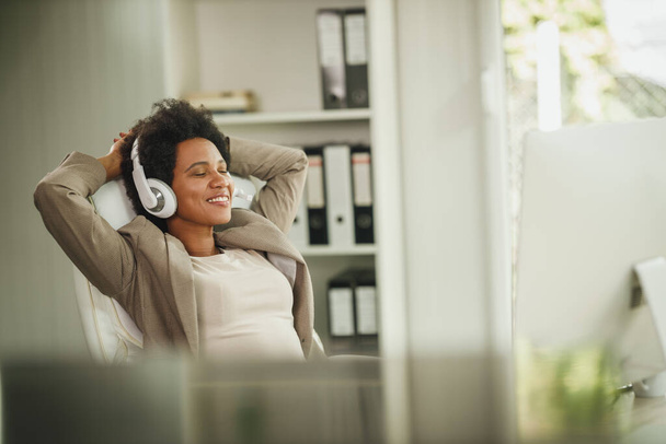 Tiro de uma mulher africana relaxando e ouvindo música nos fones de ouvido enquanto trabalhava no computador em seu escritório em casa. - Foto, Imagem