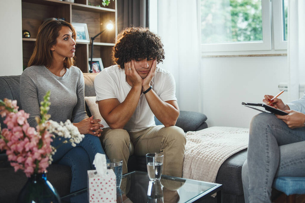 Aufnahme eines jungen Paares während einer Beratungssitzung mit ihrer Psychotherapeutin, während sie auf einem Sofa im Wohnzimmer sitzt. - Foto, Bild