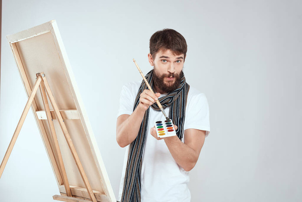 趣味の創造性の光の背景の手に筆と塗料のイーゼルに男の芸術家をペイント - 写真・画像
