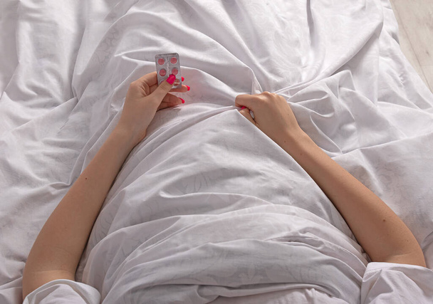 La chica enferma en la cama tiene pastillas en sus manos. Automedicación del virus. Concepto de salud - Foto, imagen