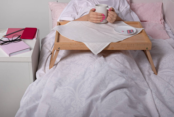 mesa portátil en la cama del paciente. Niña enferma sosteniendo una taza en la mesa móvil en la cama - Foto, imagen