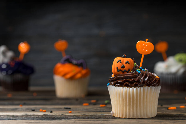 Cupcake on Halloween party. Dessert decorated with colored frosting, Icing and chocolate cream. Carved Pumpkin Jack-o-lantern and bat. Cupcakes on natural wooden background.  - Photo, Image