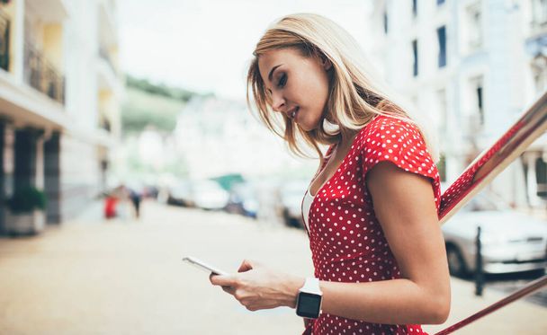 Attractive Caucasian hipster girl watching video on modern smartphone gadget connecting to 4g at urbanity, beautiful influence blogger reading application notification and received web statistics - Photo, Image