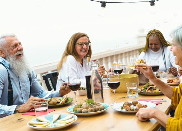 Senioren essen gemeinsam auf der heimischen Terrasse - Senioren amüsieren sich beim Abendessen auf der Hausterrasse - Konzept für Essen und Trinken - Foto, Bild