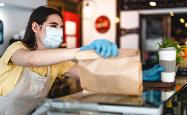 コロナウイルス発生中に注文を奪うだけで働くバーのオーナー-顔の外科マスクを身に着けている若い女性労働者が顧客にテイクアウト食事を与える-ヘルスケアとフードドリンクのコンセプト - 写真・画像