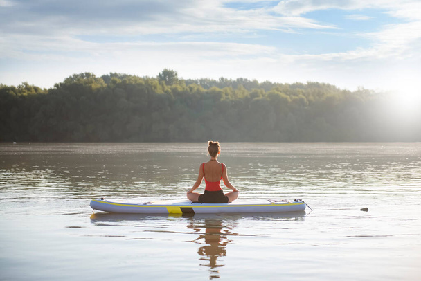 Woman meditating and practicing yoga during sunrise in paddle board - Foto, Bild
