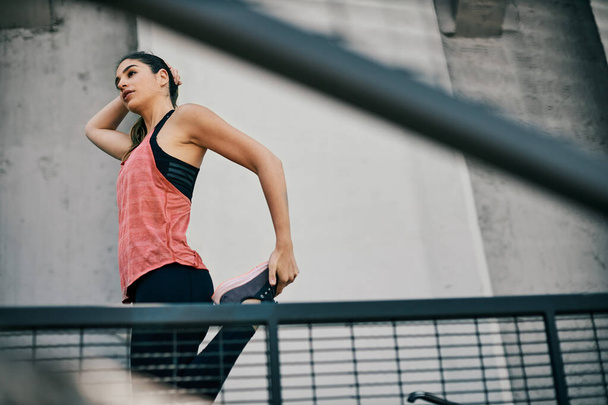 Sportswoman stretching leg before running in urban exterior. - Photo, Image