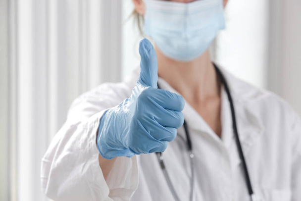 Imagem de perto do médico que usa máscara cirúrgica protetora e luvas de borracha mostrando gesto de mão polegar para cima. - Foto, Imagem