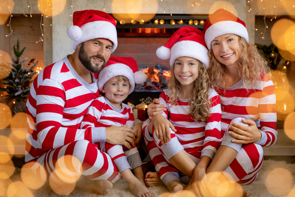 Happy family with children wearing striped pajamas near fireplace at Christmas. Mother, father and kids having fun at home. Xmas holiday concept - Photo, image