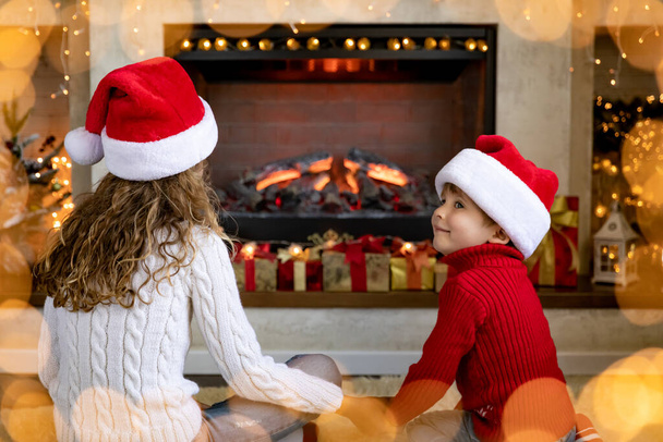 Happy children near fireplace at Christmas. Kids having fun at home. Xmas holiday concept - Fotó, kép
