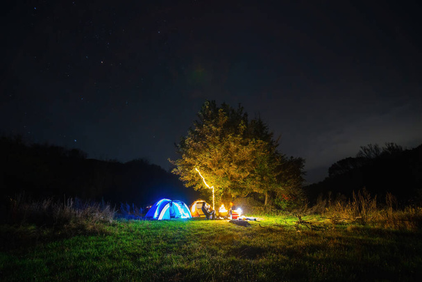 Distance Tourist camping tent garlands lighting. A night in a wilderness place. People on vacation. Active lifestyle concept and equipment for recreation and hiking. Stars, copy space - Photo, Image