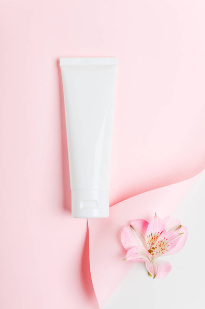 Feminine hygienic product tube on pastel pink background. Shampoo, hand cream, toothpaste white package side view on paper sheet with scroll. Skincare, facial creme, moisturizer with place for text. - Foto, Imagen