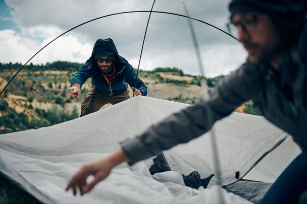 Two friends adjusting tent on rainy weather on camping trip. - Photo, Image