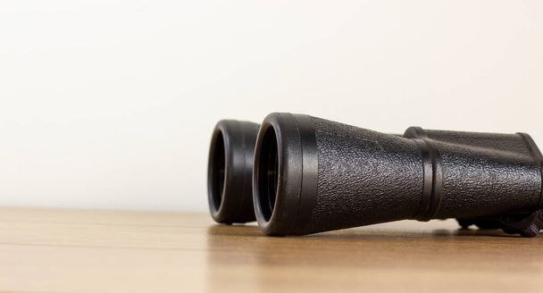 Old black binoculars on wooden table. Beautiful white background.  Copy space, concept. - Foto, imagen