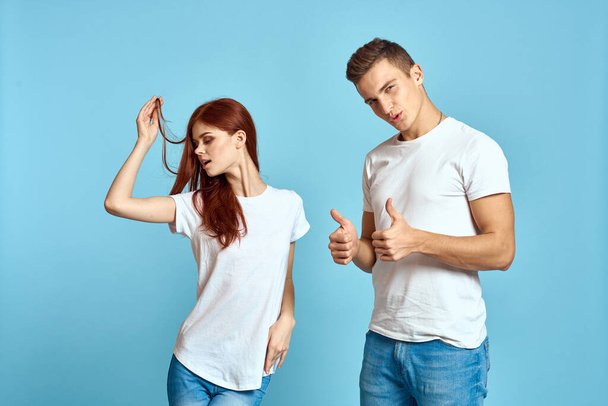 Portrait d'une fille et d'un mec sur fond bleu en T-shirts et jeans blancs vue recadrée d'amis - Photo, image
