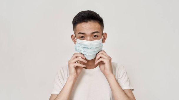 Portrait of young asian man with problematic skin wearing medical mask isolated over white background. Health care, prevention, safety concept - Photo, image