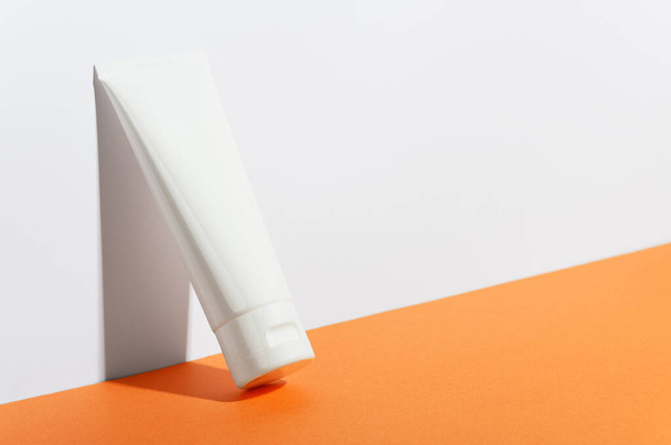 Cream tube on bright sunny orange background. Cosmetic skincare product blank plastic package. White unbranded lotion, balsam, hand creme, toothpaste mockup. Sunscreen cream bottle. - Photo, Image
