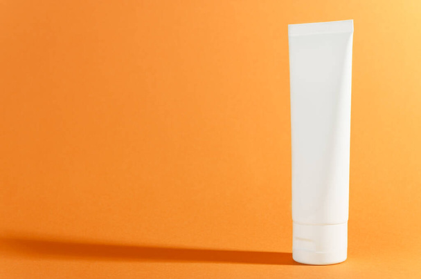 Cream tube on bright sunny orange background with shadow. Cosmetic skincare product blank plastic package. White unbranded lotion, balsam, hand creme, toothpaste mockup. Body gel, shampoo container - Фото, зображення