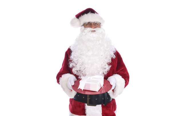 Senior man in traditional Santa Claus costume holding white wrapped present on a red tray. Isolated on white. - 写真・画像