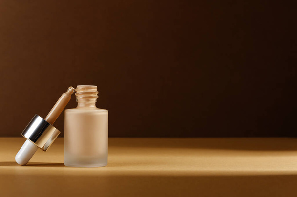 Facial foundation liquid cream for correction skin. Unbranded glass bottle with pipette on dark background. Cosmetic product for make-up. Beauty and cosmetology concept. Copy space in right side - Photo, Image