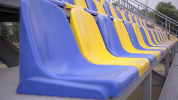 4k, prázdné plastové sedačky na stadionu. Řady žlutých a modrých sedadel na fotbalovém stadionu Tribune bez diváků a fanoušků - Záběry, video