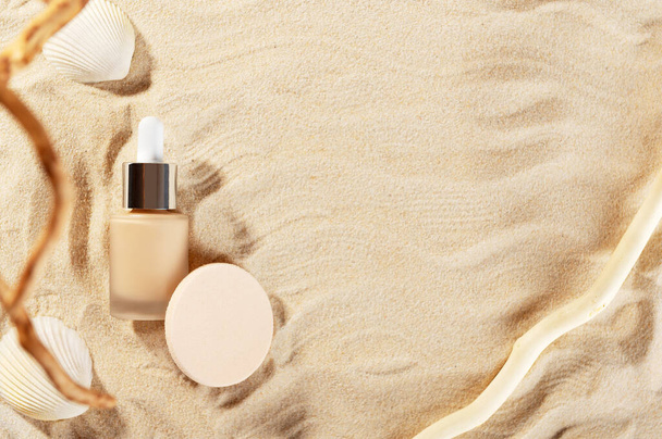 Facial foundation glass bottle cream. Closed container of liquid tone. Unbranded flacon of correction cosmetic product with cotton sponge on seashore backdrop. Beauty and cosmetology branding concept. - Photo, Image