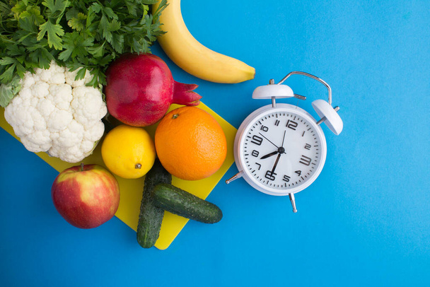 Draufsicht auf weißen Wecker, Gemüse und Obst auf blauem Hintergrund - Foto, Bild